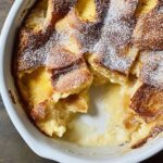 Homemade bread pudding cut into squares in white ceramic dish revealing soft custardy texture with golden brown top