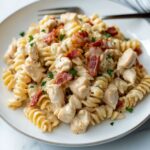 Close-up of creamy chicken bacon ranch pasta with rotini, bacon bits, and chopped parsley served on a white plate with a fork.