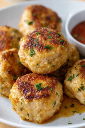 Chicken meatballs recipe showing golden-brown seared meatballs with fresh parsley garnish in cast iron skillet
