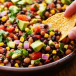 Cowboy caviar recipe showing colorful bean and vegetable mixture with tortilla chip being dipped into fresh salad