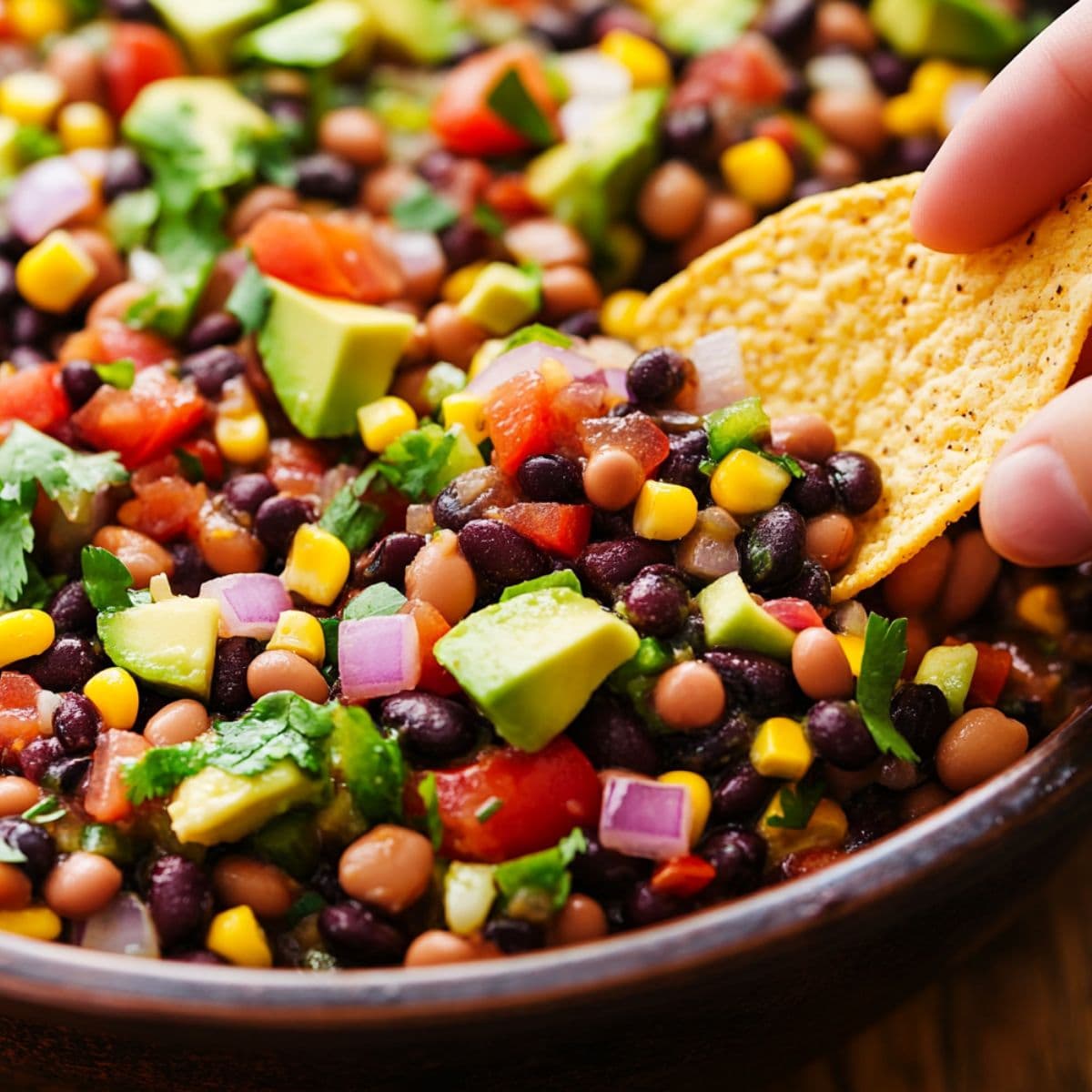 Cowboy caviar recipe showing colorful bean and vegetable mixture with tortilla chip being dipped into fresh salad
