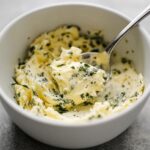 Creamy homemade garlic butter with fresh parsley in white bowl being mixed with spoon