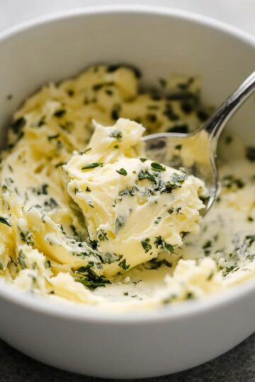 Creamy homemade garlic butter with fresh parsley in white bowl being mixed with spoon