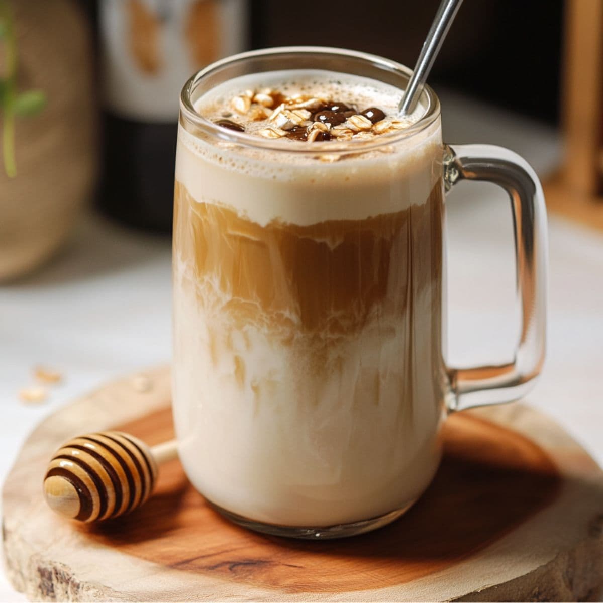 Perfect honey oat milk latte in clear glass mug showing beautiful golden layers, topped with honey drizzle and foam, styled with honey dipper on wooden board