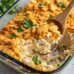 Million dollar chicken casserole in glass baking dish showing golden cracker topping and creamy chicken mixture with wooden serving spoon