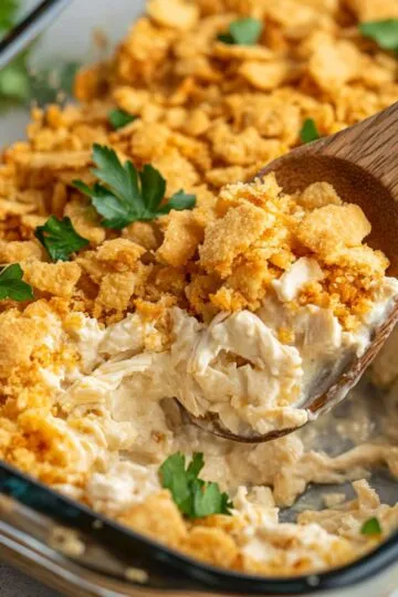 Million dollar chicken casserole in glass baking dish showing golden cracker topping and creamy chicken mixture with wooden serving spoon