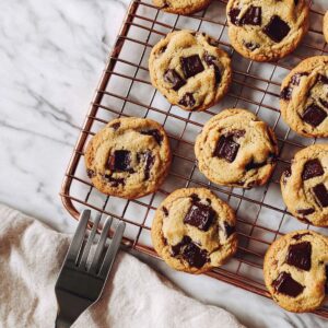 Perfect thick chocolate chip cookies with golden brown edges and melted chocolate chunks cooling on copper wire rack with spatula, showing ideal bakery-style texture