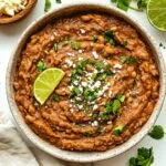 Refried beans recipe showing creamy homemade Mexican beans garnished with fresh cilantro, lime wedge and cotija cheese in rustic bowl
