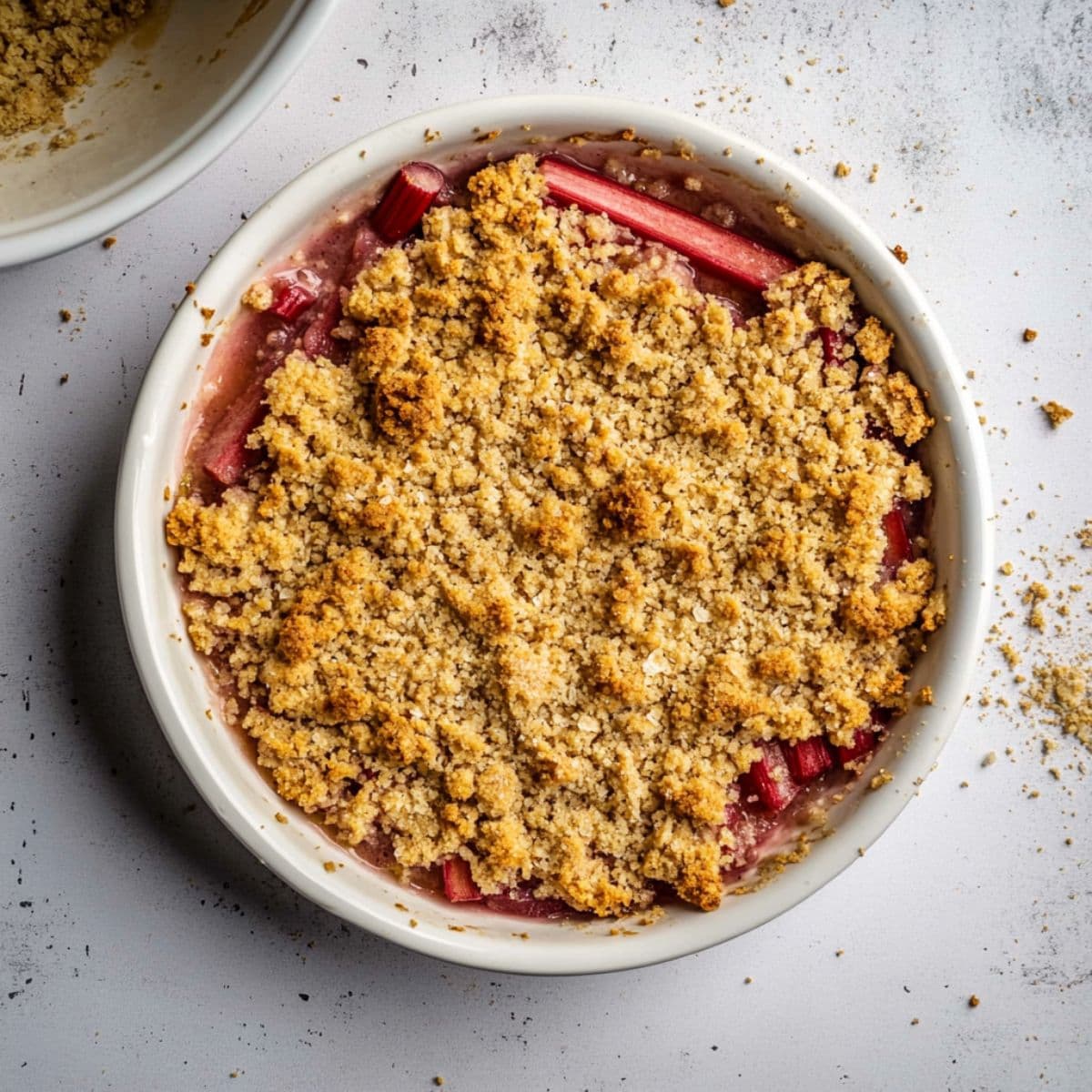 Unbaked rhubarb crisp in a white baking dish, with fruit filling at the bottom and crumble topping on top.