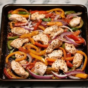 Raw chicken strips with colorful bell peppers and onions on a sheet pan for fajitas prep