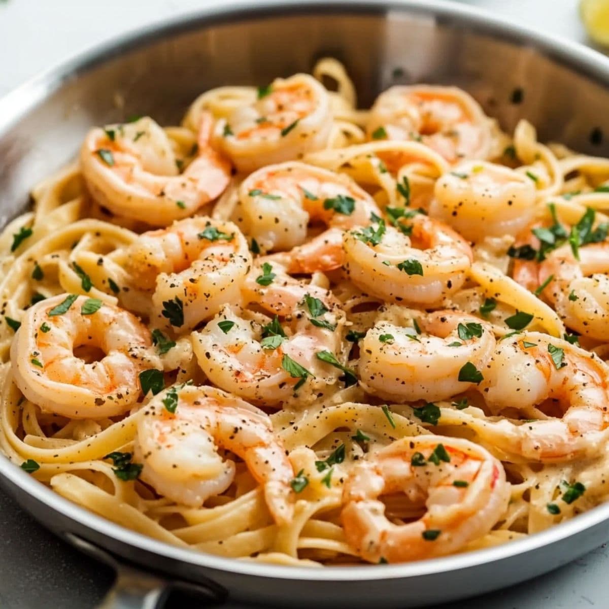Shrimp pasta mixed with creamy sauce, garnished with chopped parsley in a stainless steel pan.