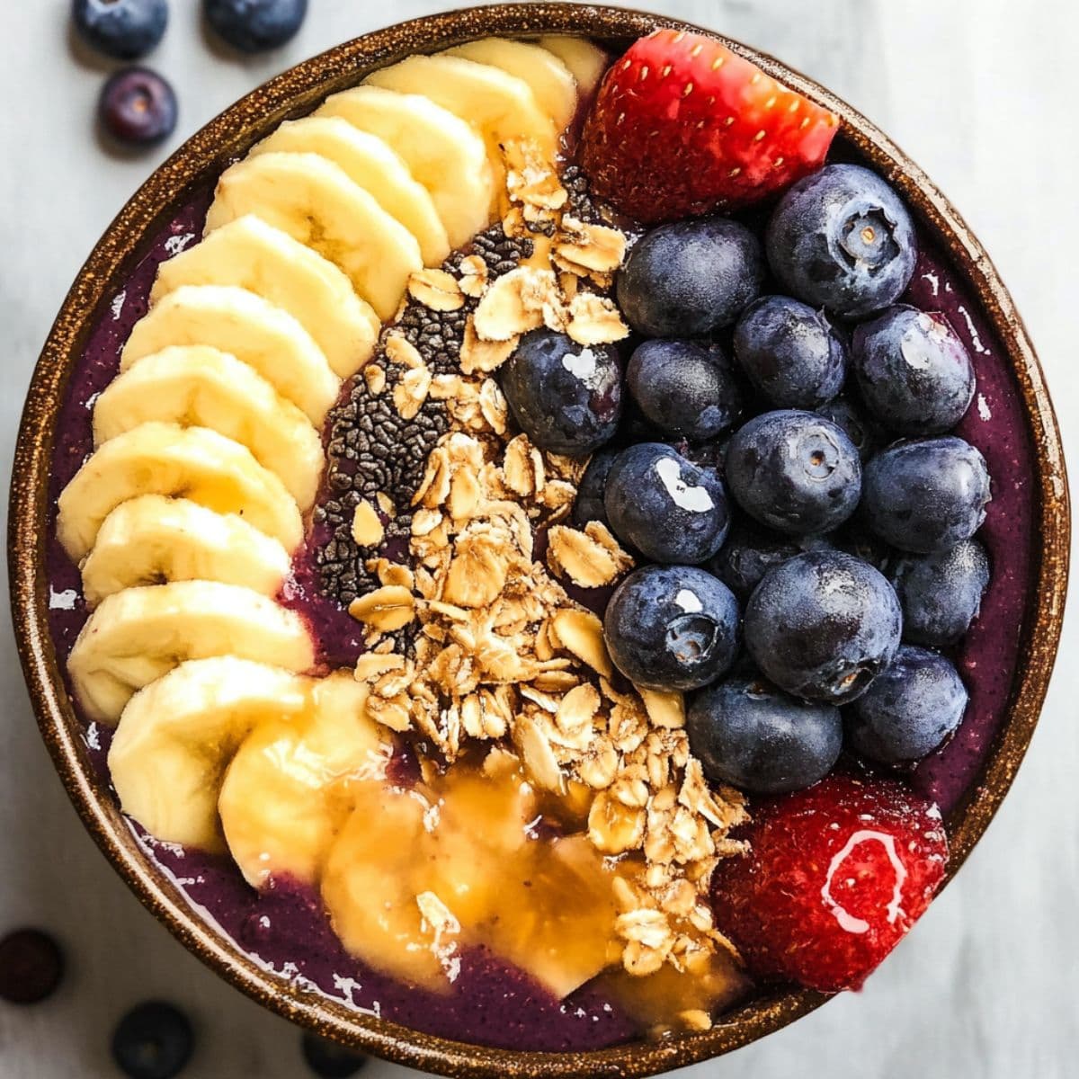 Acai bowl recipe with vibrant purple base topped with banana slices blueberries strawberries and granola