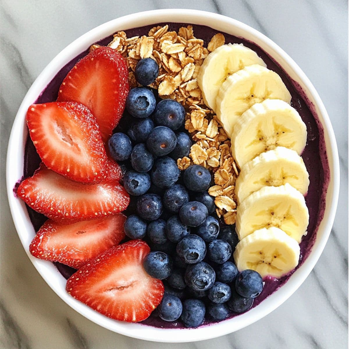 Acai bowl served with fresh strawberries blueberries banana slices and granola in white bowl