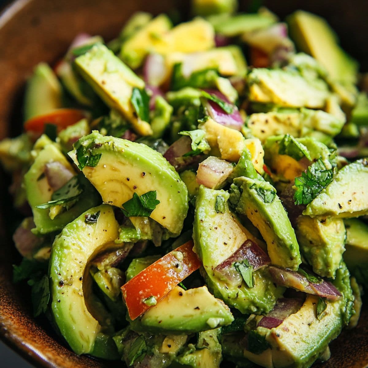 Fresh avocado salad with cucumber, red onion, and herbs in wooden bowl with lime dressing