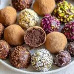 Assorted homemade chocolate truffles with various coatings including cocoa powder, coconut, nuts and colorful sprinkles arranged on white plate