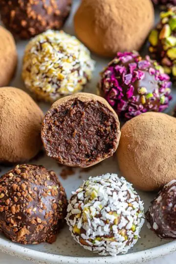 Assorted homemade chocolate truffles with various coatings including cocoa powder, coconut, nuts and colorful sprinkles arranged on white plate