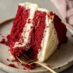 Classic red velvet cake slice with fluffy red layers and cream cheese frosting on ceramic plate with gold fork
