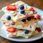 Yogurt bark stacked pieces with mixed berries, nuts and colorful toppings on white plate