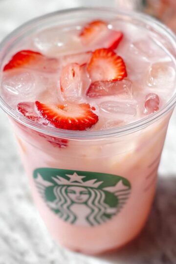 Pink drink starbucks recipe in clear glass with ice, fresh strawberries and starbucks logo