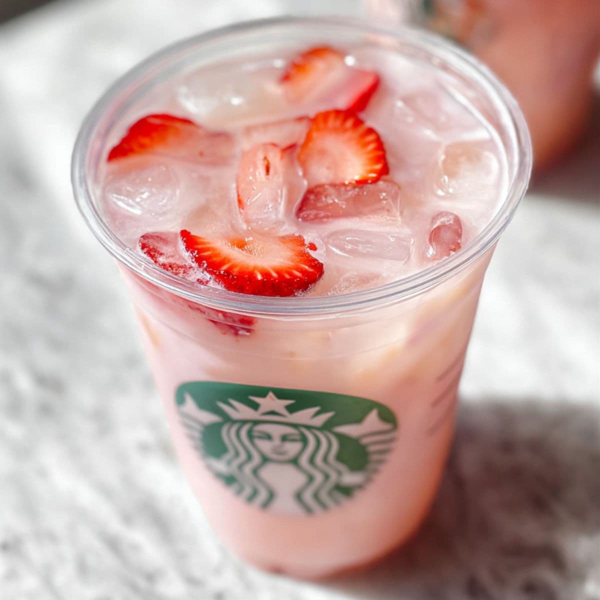 Pink drink starbucks recipe in clear glass with ice, fresh strawberries and starbucks logo