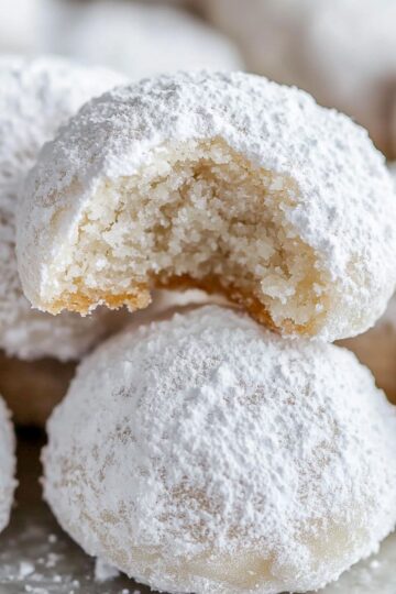 Snowball cookies covered in powdered sugar with one cookie broken in half showing crumbly texture