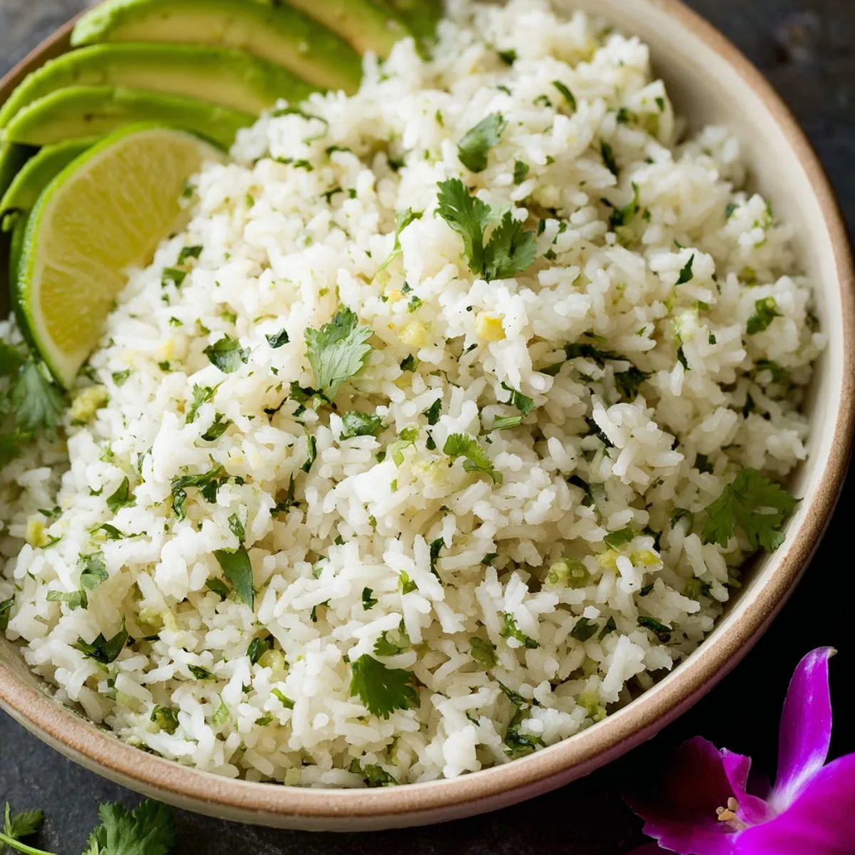 Cilantro lime rice served in a wooden bowl with fresh lime wedges, sliced avocado, and cilantro garnish on a dark surface