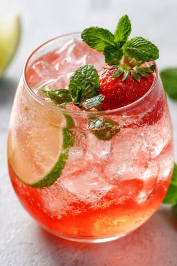 Agua fresca strawberry drink with fresh mint, lime and ice in glass, refreshing Mexican summer beverage recipe