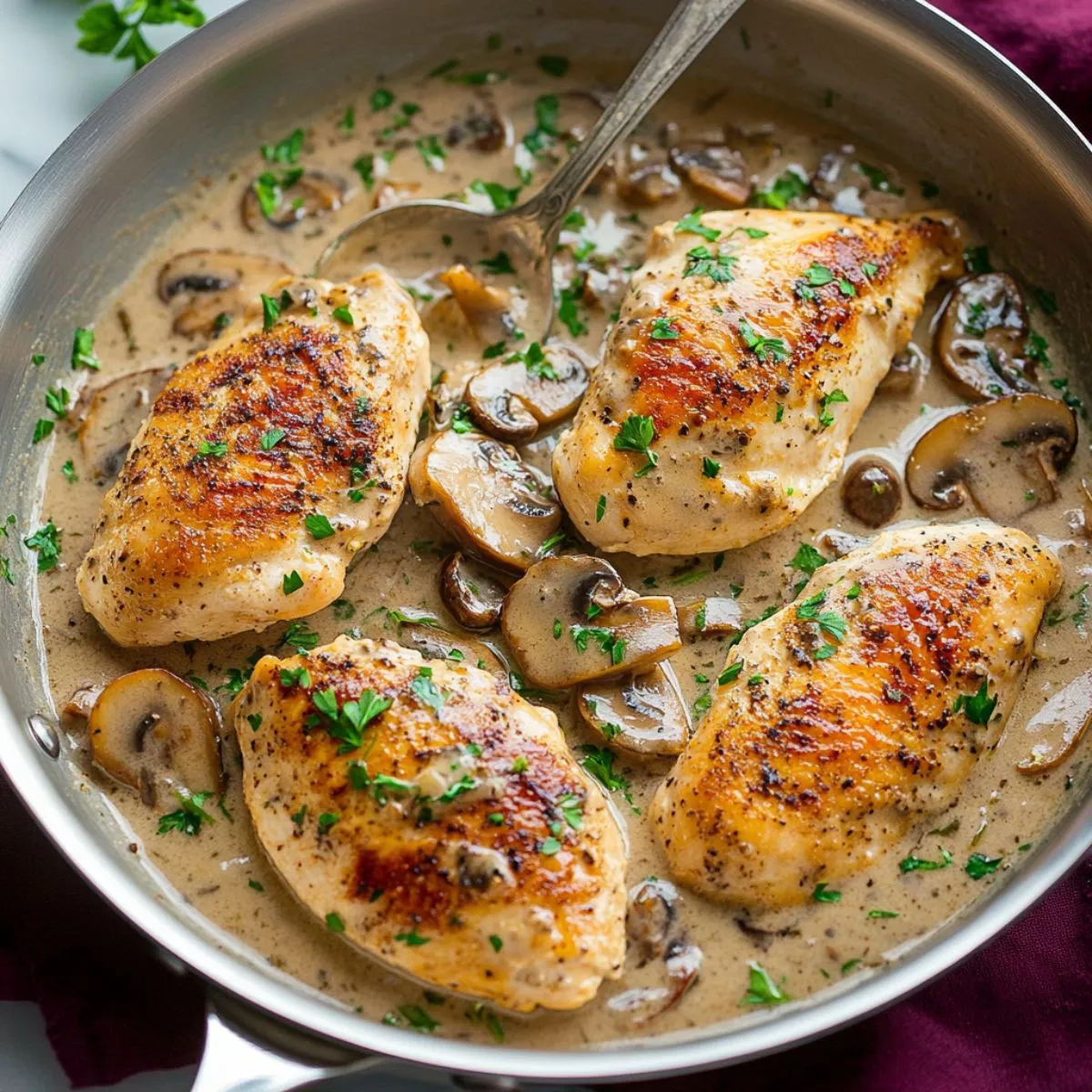 Chicken marsala in stainless steel skillet showing golden-brown seared chicken breasts in creamy Marsala wine sauce with sautéed mushrooms and fresh parsley garnish displaying restaurant-quality Italian cuisine presentation
