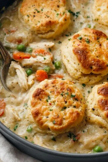 Chicken pot pie with biscuits in a cast iron skillet showing golden brown biscuits on top of creamy chicken and vegetable filling with fresh herbs sprinkled on top