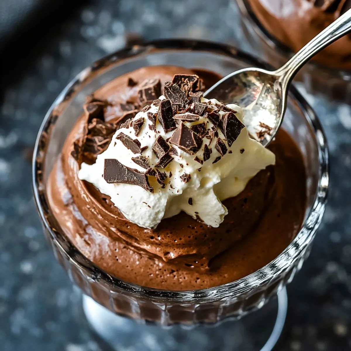 Chocolate mousse recipe in elegant glass bowl topped with whipped cream and dark chocolate shavings with silver spoon