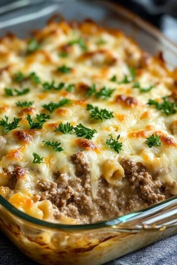Hashbrown casserole in glass baking dish with golden melted cheese top and ground beef layers garnished with fresh parsley