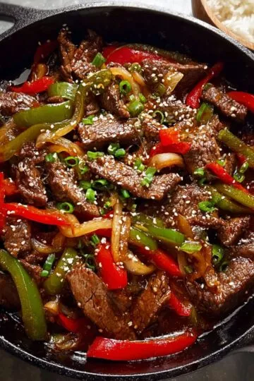 Pepper steak recipe with tender beef strips and colorful bell peppers in savory sauce served in cast iron skillet