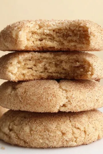 Protein cookies stacked showing soft chewy texture with cinnamon coating and one cookie broken in half revealing tender interior crumb