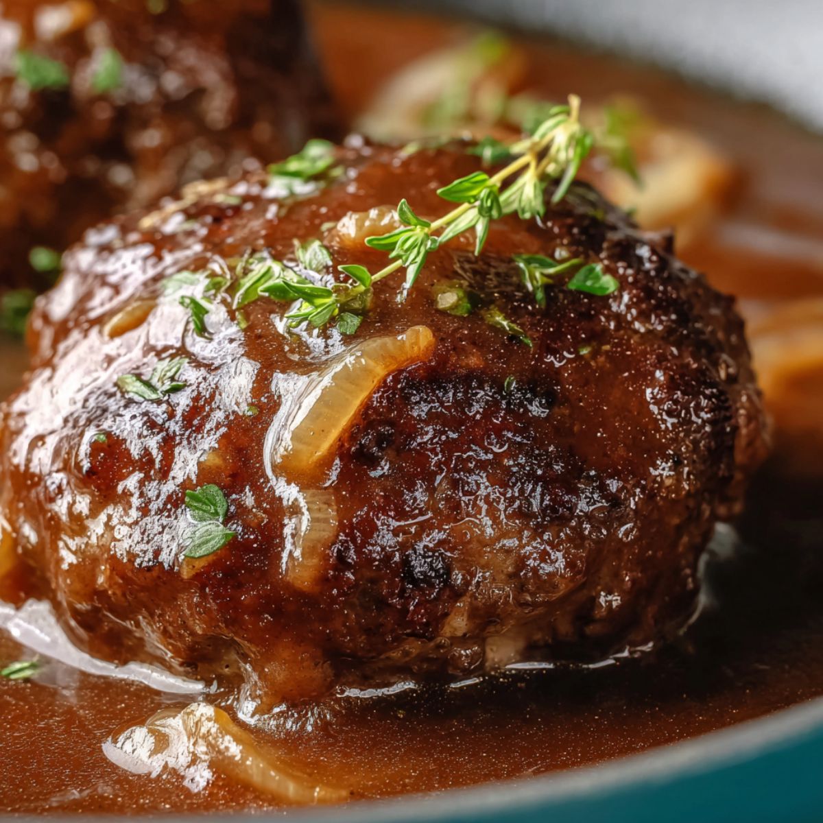 salisbury steak recipe close-up of a juicy ground beef patty smothered in rich brown onion gravy and garnished with fresh thyme.