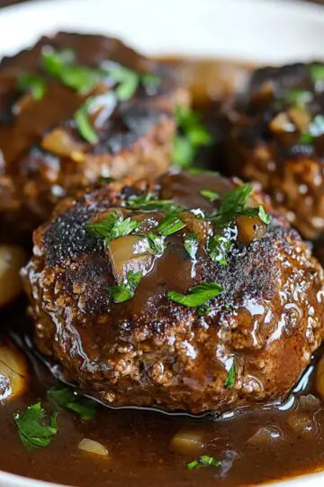Salisbury steak patties in white serving dish showing perfectly glazed beef with rich brown mushroom and onion gravy, fresh parsley garnish and caramelized onions displaying homemade comfort food presentation
