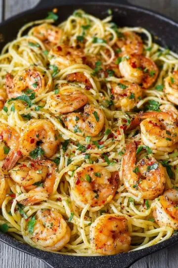 Shrimp pasta with garlic butter sauce and fresh parsley in black cast iron skillet showing golden seared shrimp over linguine noodles