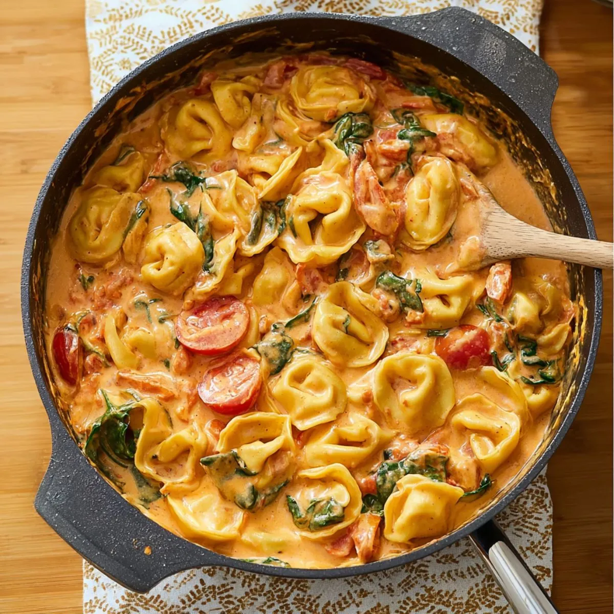Tortellini in creamy garlic sauce with spinach and tomatoes cooking in cast iron skillet on wooden table