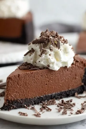 Baileys cheesecake slice showing smooth Irish cream filling on chocolate cookie crust with whipped cream and chocolate shavings on white plate