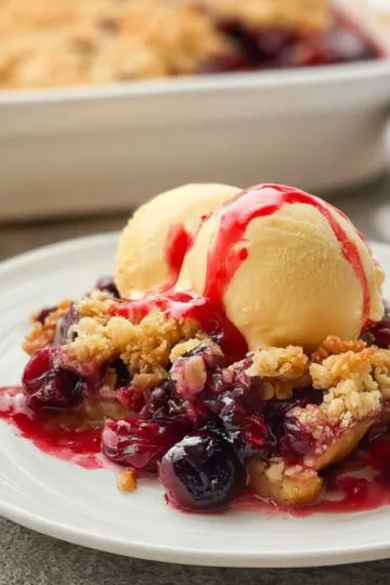Cherry dump cake slice on white plate with vanilla ice cream showing golden cake layer bubbling cherry filling and fresh cherry sauce