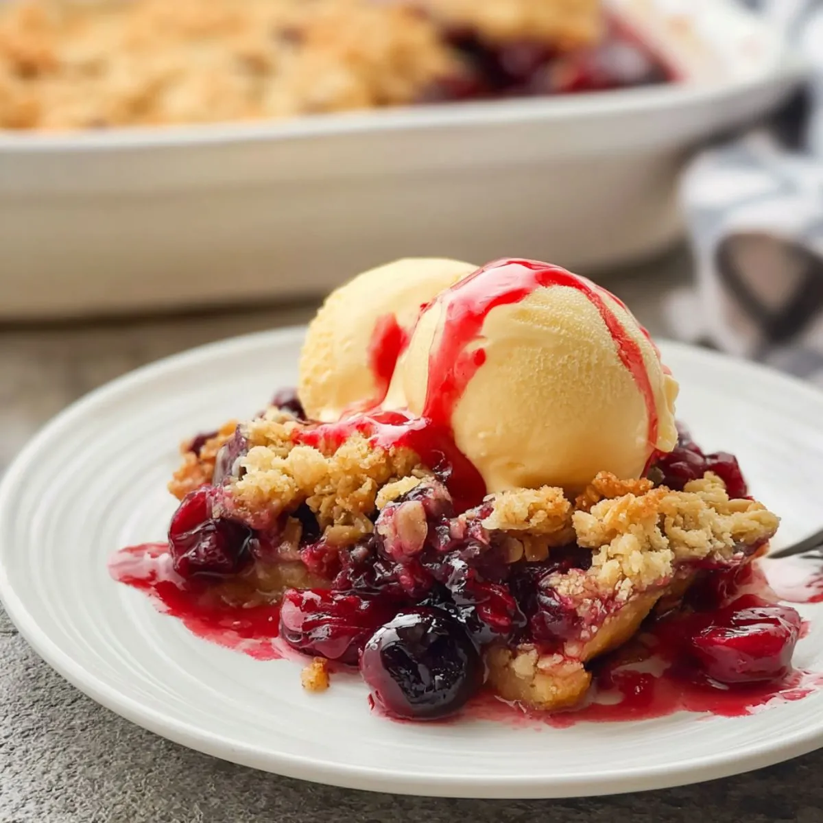 Cherry dump cake slice on white plate with vanilla ice cream showing golden cake layer bubbling cherry filling and fresh cherry sauce