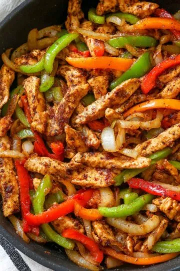 Chicken fajita recipe with seasoned chicken strips and colorful bell peppers and onions sizzling in cast iron skillet showing caramelized edges and vibrant colors