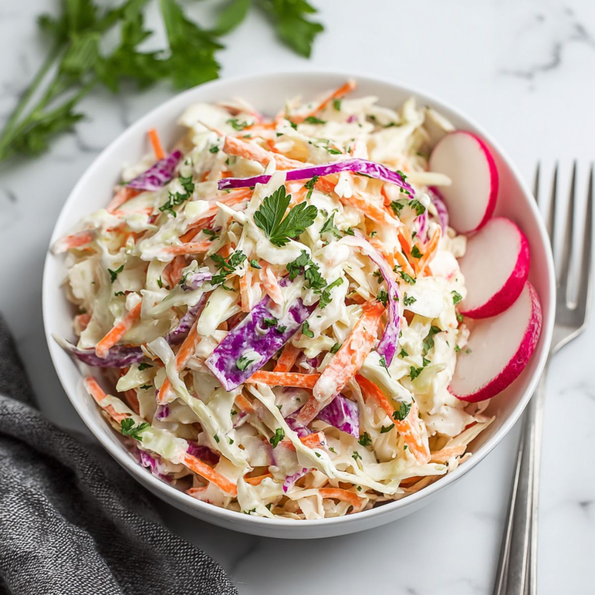 Coleslaw recipe showing fresh colorful mix of shredded green and purple cabbage with julienned carrots in creamy dressing garnished with fresh parsley and sliced radishes in white bowl