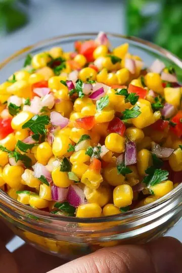 Corn salsa close-up showing bright yellow kernels mixed with diced red peppers, purple onions, and fresh cilantro in clear glass bowl