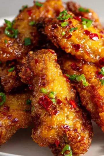Crispy bang bang chicken pieces with golden brown coating, sweet chili sauce glaze, and fresh green onions garnish on a white plate showing perfectly crispy texture and glossy sauce coating