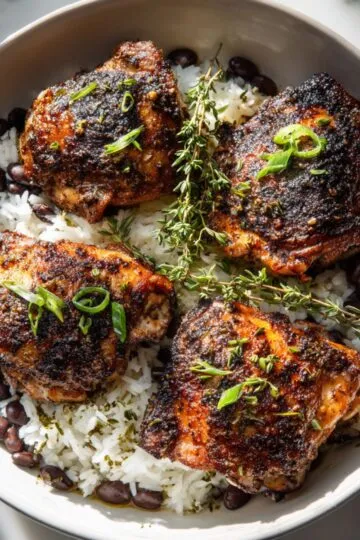 Jerk chicken recipe grilled thighs with dark spice crust served over coconut rice and black beans with fresh thyme garnish
