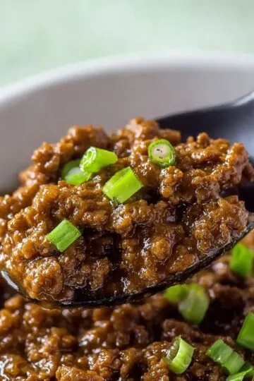 Mongolian beef glazed with sweet savory sauce on a spoon with green onion garnish