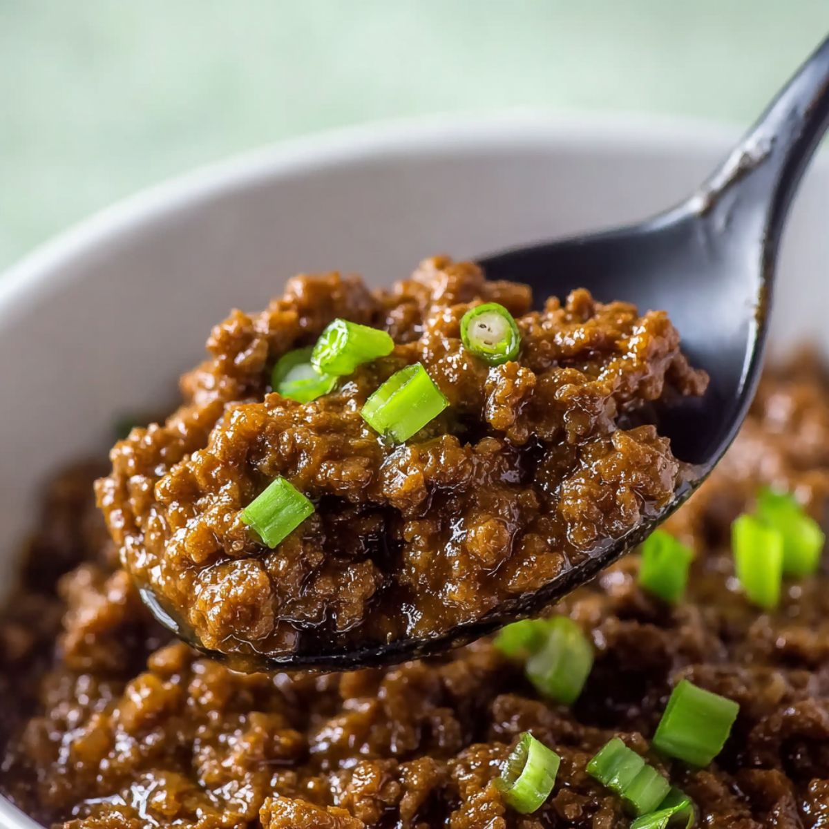 Mongolian beef glazed with sweet savory sauce on a spoon with green onion garnish