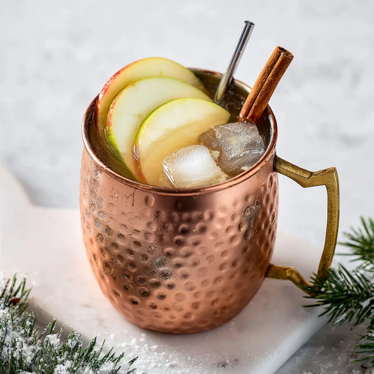 Moscow mule recipe with apple slices and cinnamon sticks in hammered copper mug with ice on winter background