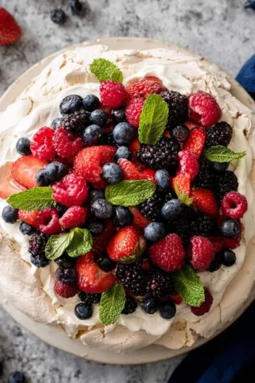 Pavlova crispy meringue dessert topped with fresh mixed berries strawberries blueberries raspberries and mint leaves on white cream