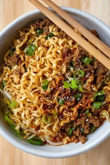 Ramen noodles bowl with ground meat, green onions, sesame seeds, and chopsticks in ceramic bowl showing upgraded instant noodles
